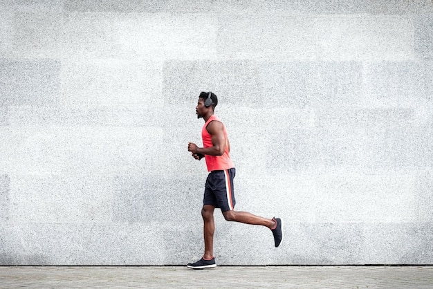 Афроамериканский бегун быстро бежит вперед на фоне городской стены