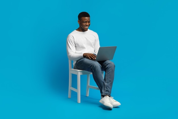 African american guy sitting on chair and using modern notebook