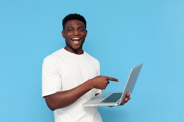 african american guy in white tshirt uses laptop and smiles on blue isolated background man points