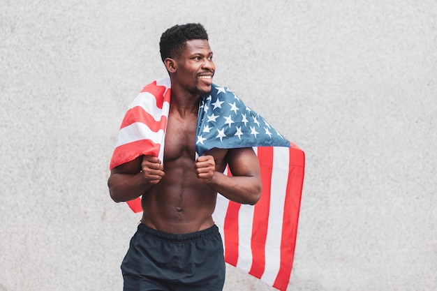 African american guy with usa flag smiles and rejoices against wall background july 4