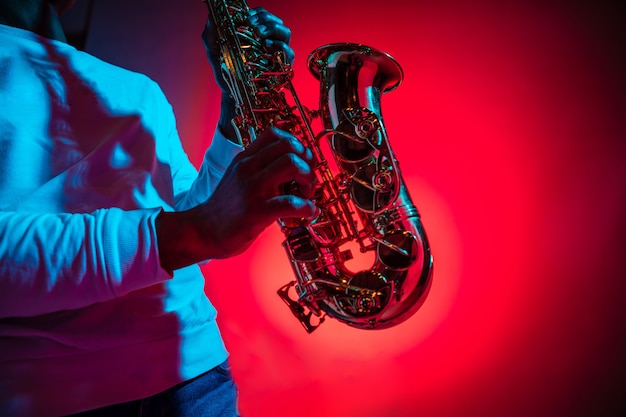 African American handsome jazz musician playing the saxophone in the studio on a neon background. Music concept. Young joyful attractive guy improvising. Close-up retro portrait.