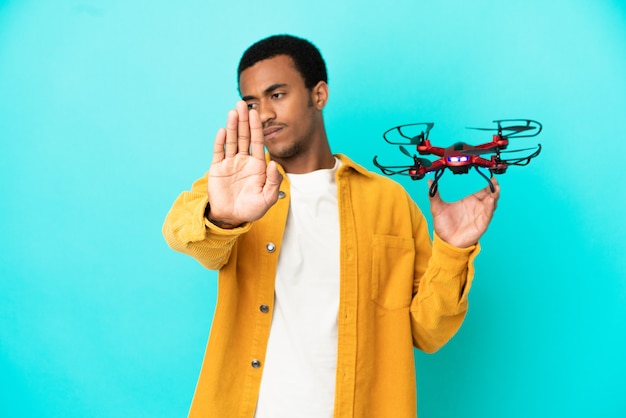 African American handsome man holding a drone over isolated blue background making stop gesture and disappointed