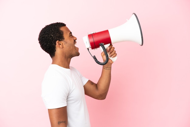 African American handsome man on isolated pink background shouting through a megaphone to announce something in lateral position