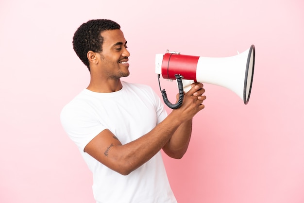 Афро-американский красавец на изолированном розовом фоне кричит в мегафон, чтобы что-то объявить