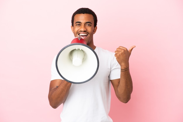 Афро-американский красавец на изолированном розовом фоне кричит в мегафон и указывает сторону