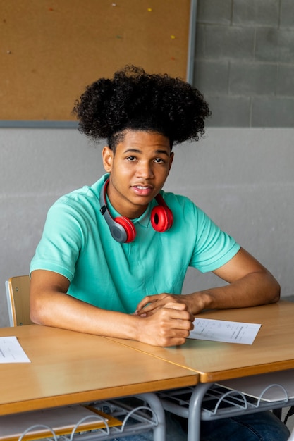 Studente di liceo afroamericano seduto dietro la scrivania in classe guardando la telecamera istruzione