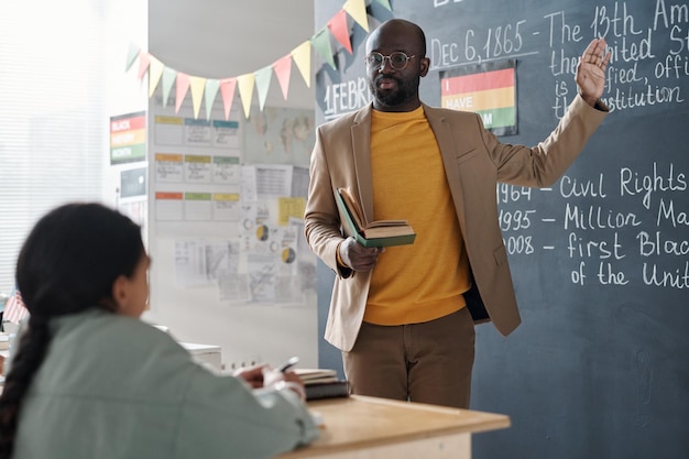 African American history teacher pointing at blackboard and telling about history to his students