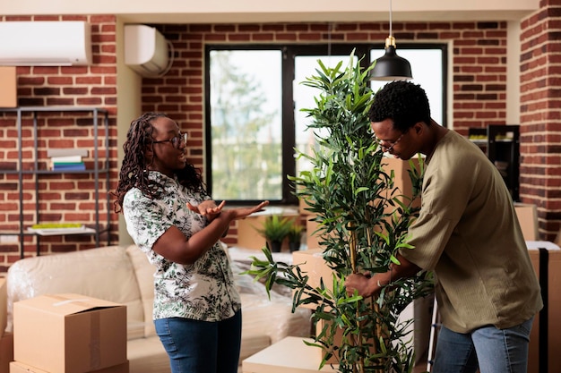 アフリカ系アメリカ人の住宅所有者は、引っ越しのために新しいアパートを飾り、リビングルームで植物や家具を開梱します。一緒に最初の家を購入した後の世帯の移転、ライフイベント。