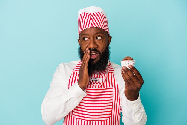 African american ice cream maker man holding an ice cream isolated on blue background is saying a secret hot braking news and looking aside