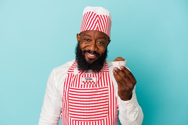 Афро-американский производитель мороженого человек, держащий мороженое на синей стене, счастливый, улыбающийся и веселый.