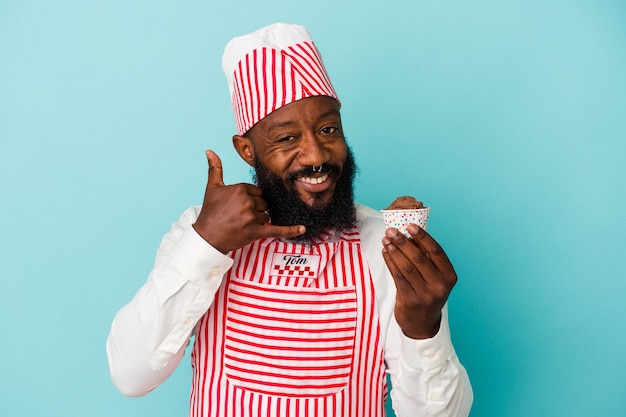 African american ice cream maker man holding an ice cream isolated on blue wall showing a mobile phone call gesture with fingers.