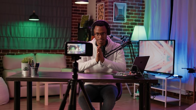 Афро-американский влиятельный человек записывает подкаст с помощью цифровой видеокамеры для публикации в блоге в социальных сетях. Создатель контента транслирует онлайн-шоу в прямом эфире из домашней студии с использованием профессионального оборудования.