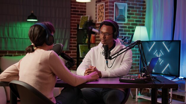 African american internet show host interviewing famous influencer for social media podcast in home recording studio. Content creator talking in interview with presenter using professional microphone.