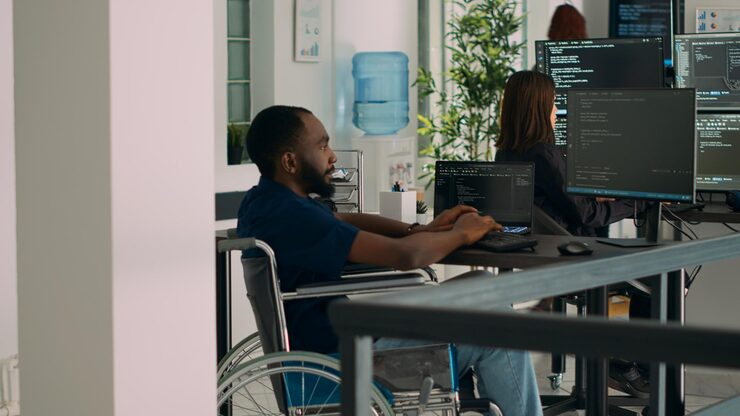 Photo african american it engineer with disability typing code in it development agency office, using terminal window to write html script database. wheelchair user working with security programming.