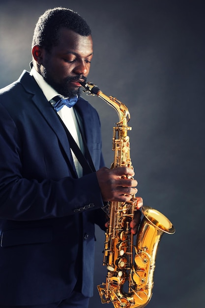 African American jazz musician playing the saxophone on grey background