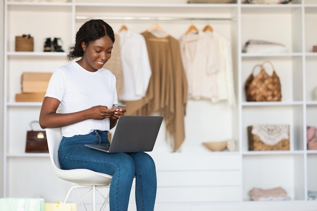 African american lady using laptop and smartphone shopping at home