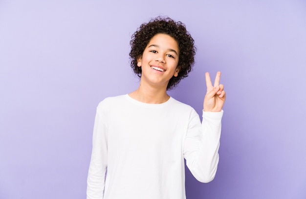 African american little boy isolated joyful and carefree showing a peace symbol with fingers.