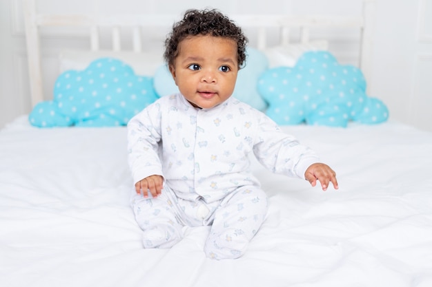 Афро-американский маленький ребенок на белой кровати в спальне лежит в пижаме