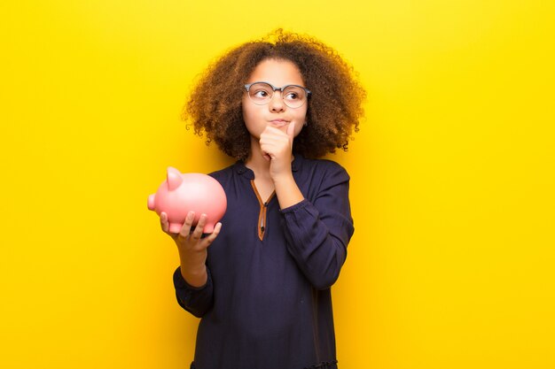 African american little girl  against flat wall holding a piggy bank