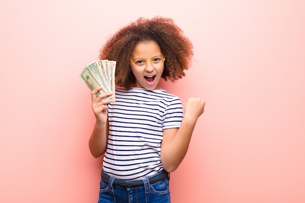 African american little girl  against flat wall with dollar banknotes