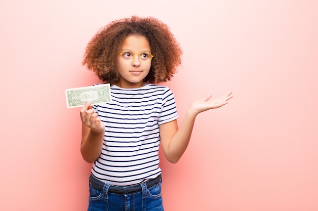 Bambina afroamericana contro la parete piana con le banconote del dollaro