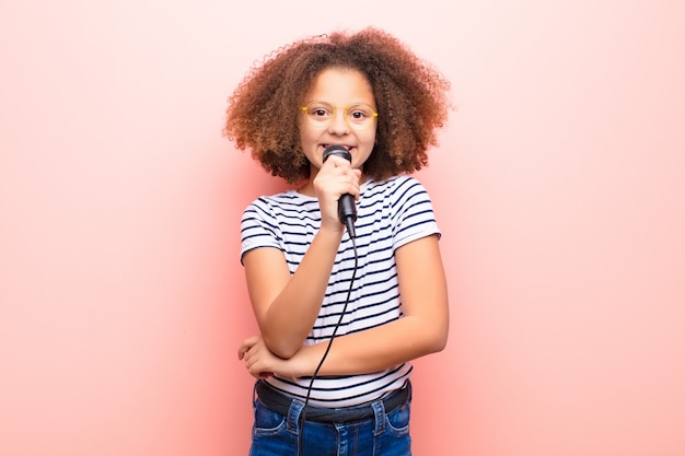 Bambina dell'afroamericano contro la parete piana con un microfono