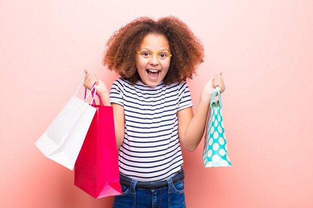 Photo african american little girl  against flat wall with shopping bags