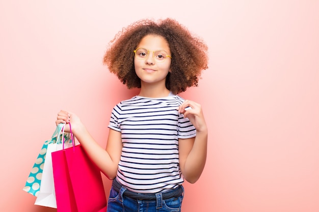 Bambina afroamericana contro la parete piana con le borse della spesa