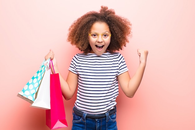 Photo african american little girl  against flat wall with shopping bags