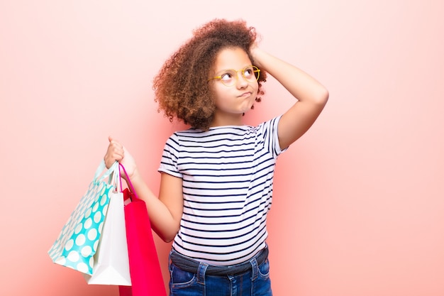 Photo african american little girl  against flat wall with shopping bags