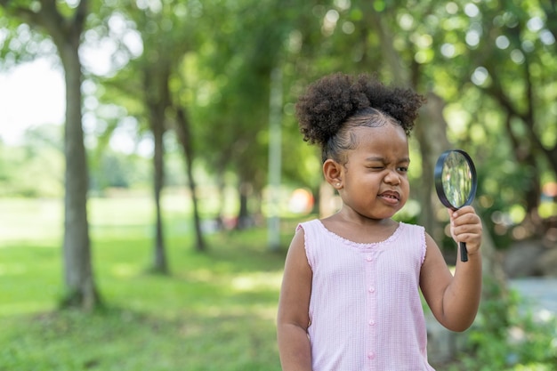 African American little girl learning and looking into magnifying glass in her hand in park