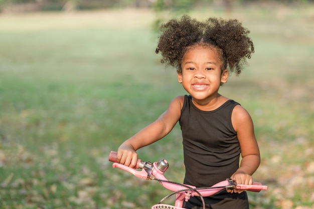 African American little girl smiling and looking at camera while riding a bicycle in the park