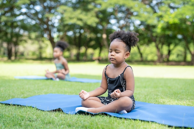 African American little girls their eyes closed sitting on roll mat practice meditation yoga in park