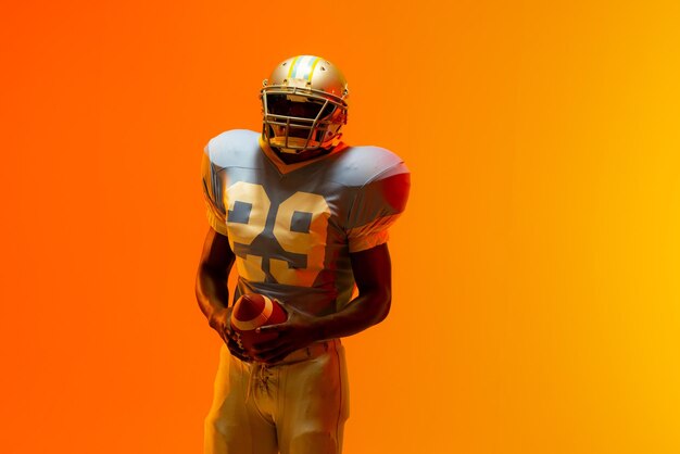 Photo african american male american football player holding ball with neon orange lighting