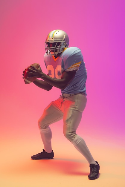 African american male american football player holding ball with neon pink lighting
