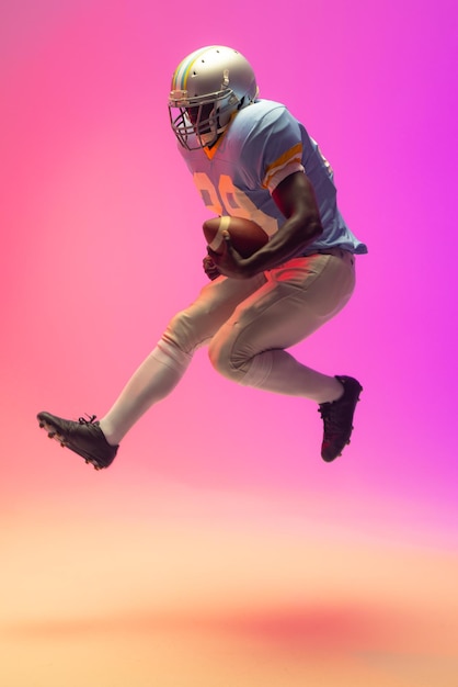 African american male american football player holding ball with neon pink lighting