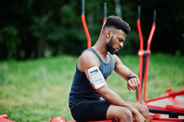 Uomo sportivo atleta maschio afroamericano con custodia per braccio sportivo da corsa per telefono cellulare che fa esercizi sui simulatori di allenamento per strada