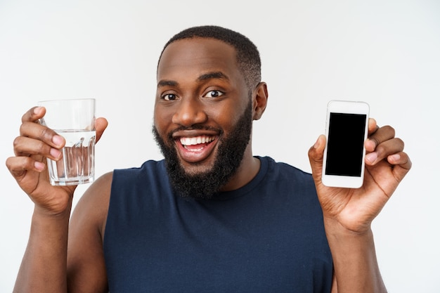 Uomo di sport dell'atleta maschio afroamericano con gli sport correnti con il telefono cellulare e l'acqua potabile da vetro.