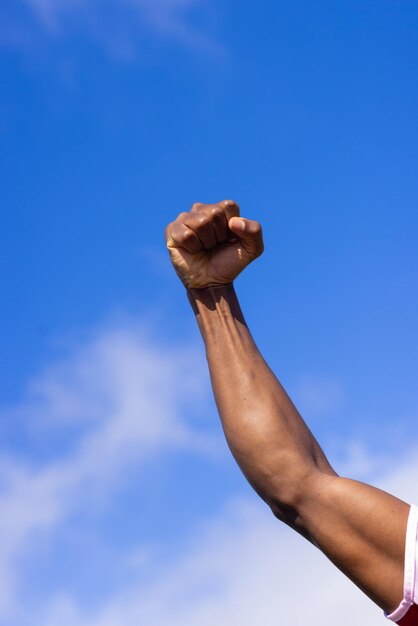 Photo african american male athlete with fist raised under blue sky on field