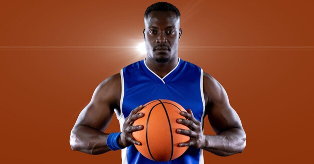 African american male basketball player holding basketball against spot of light in background