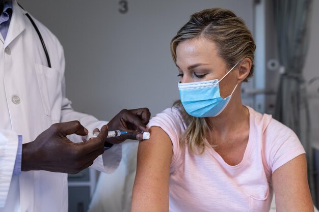 Foto medico maschio afroamericano che vaccina il paziente caucasico in ospedale