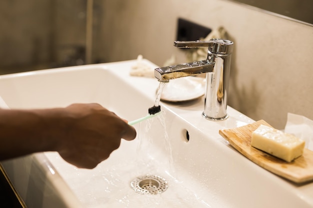 African american male hand holding toothbrush with toothpaste applied on it in bathroom Close up of man hand ready for brushing teeth Guy hand holding toothbrush with white tooth paste