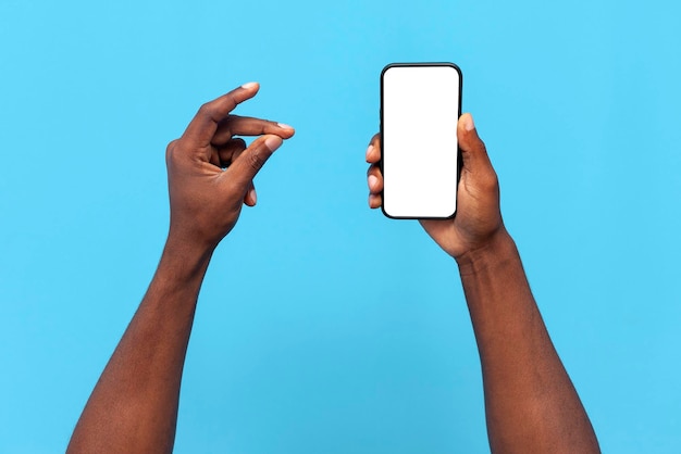 アフリカ系アメリカ人の男性の手は空白のスマートフォン画面を示し、青い背景に指を鳴らします