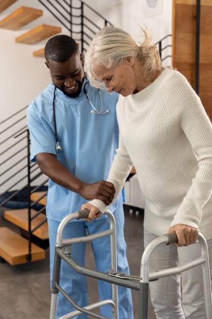 写真 アフリカ系アメリカ人の男性医療従事者が白人の年配の女性が歩行器で歩くのを手伝う