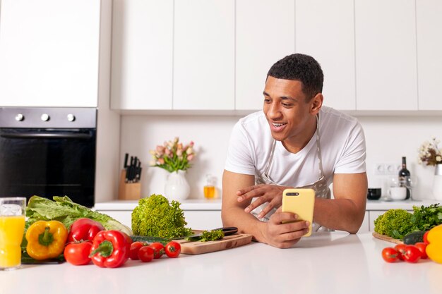 Африканско-американский мужчина в фартуке готовит вегетарианский салат с овощами и зеленчуком на современной кухне