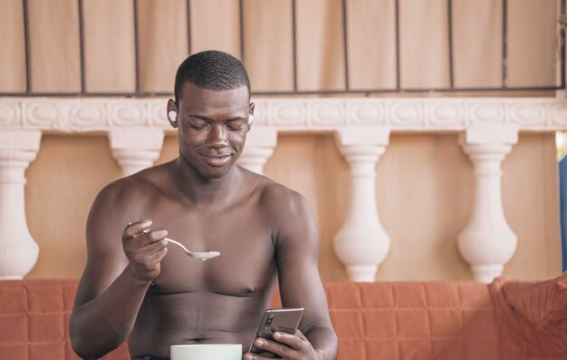 アフリカ系アメリカ人男性が朝食をとりながらスマートフォンを閲覧