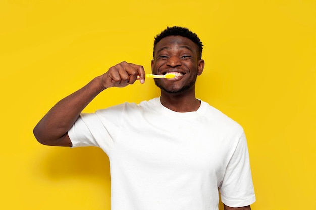 african american man brushing his teeth with toothbrush on yellow isolated background