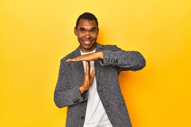 African American man in casual blazer yellow studio showing a timeout gesture