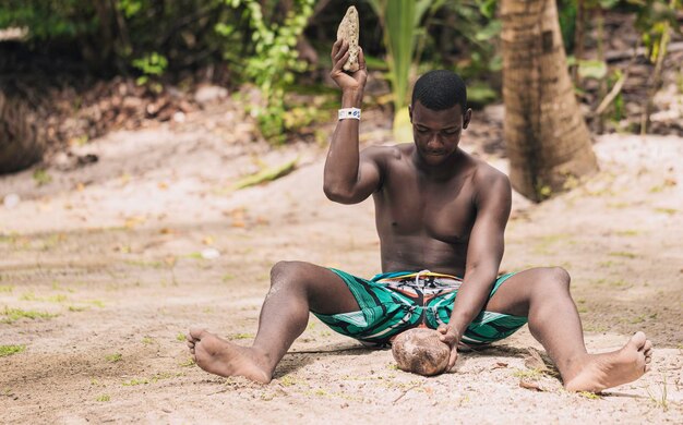 African American man cracking open a coconut with a stone