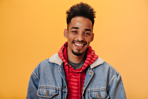 Uomo afroamericano in giacca di jeans sorridente sul muro arancione orange